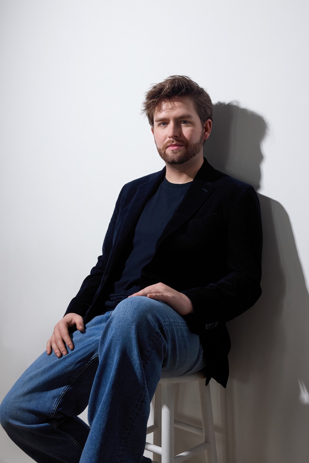 Patrick Brown — seated on stool, blazer and jeans, studio